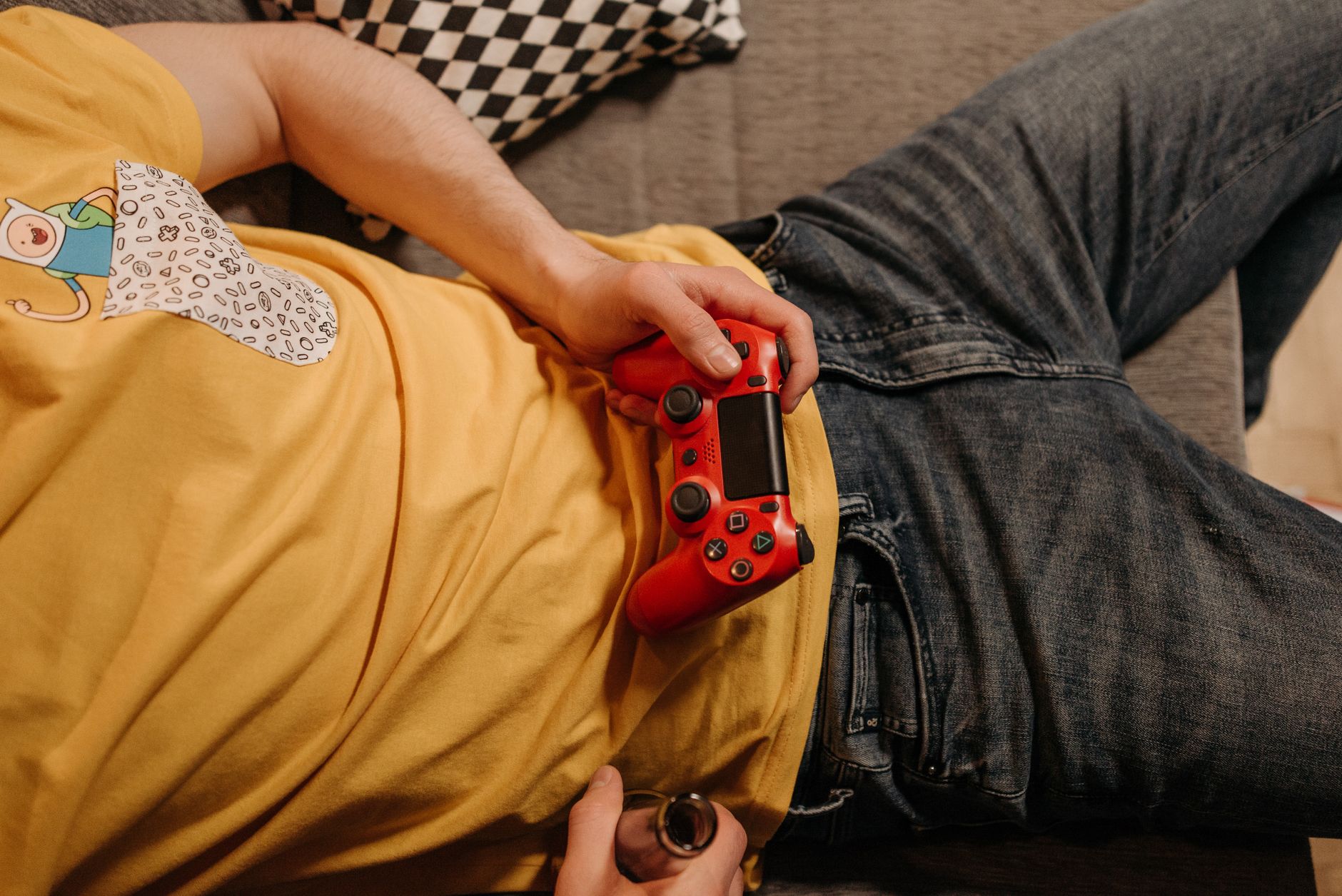 Person holding a red game controller while relaxing on a couch in comfortable clothes.