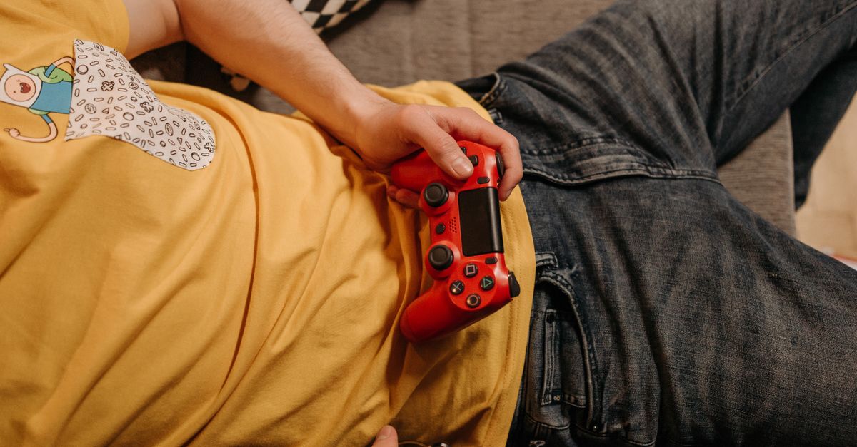 Person holding a red game controller while relaxing on a couch in comfortable clothes.