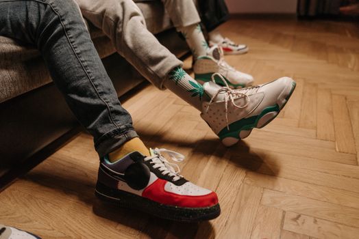 Close-up of legs in colorful sneakers relaxing indoors on wooden floor.