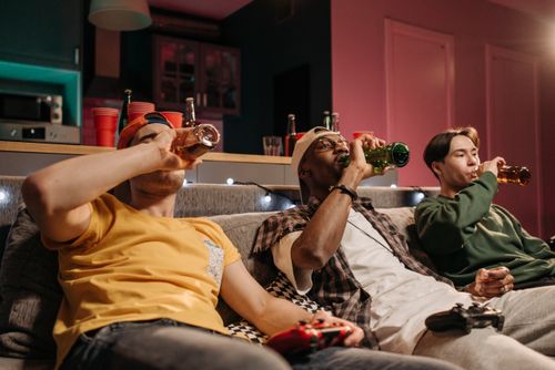 Free Three friends relaxing with drinks and gaming on a cozy indoor couch setting. Stock Photo