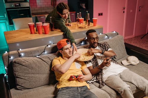 Free Three friends relax indoors, enjoying video games and snacks, creating a fun and social atmosphere. Stock Photo