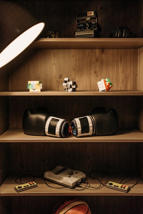 A Pair of Black Boxing Gloves on Wooden Shelves with Game Console