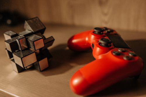 Free Close-up of a red game controller and 3D cube puzzle on a wooden surface. Stock Photo