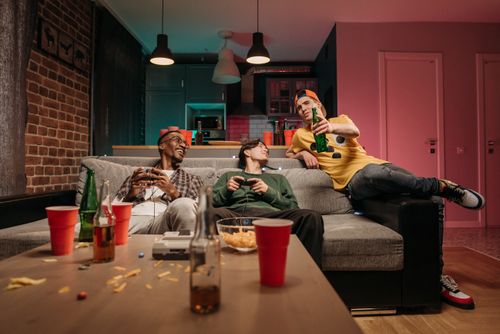 Free Group of friends enjoying a gaming session with drinks in a cozy home setting. Stock Photo