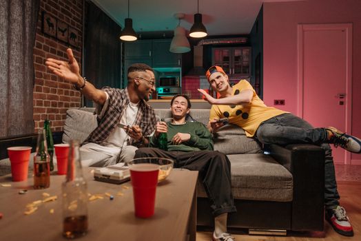 Three friends having fun at home playing games and enjoying drinks together.