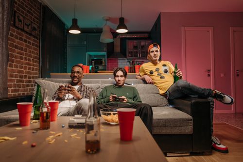 Free Three friends playing video games in a cozy living room with snacks and drinks. Stock Photo