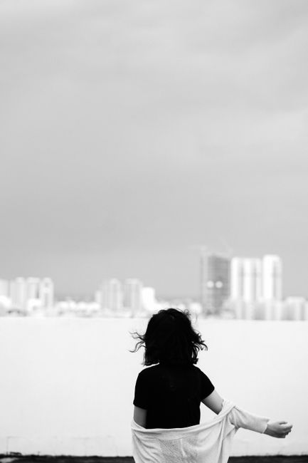 Black and white back view of dark haired female standing near railing and looking at blurred cityscape