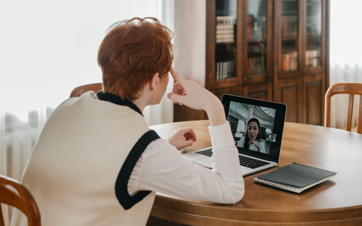 A man sitting at a table, using a laptop for a video call, set in a cozy indoor space.