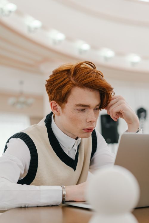 Free Young adult with red hair intensely working on a laptop in a well-lit, elegant setting. Stock Photo