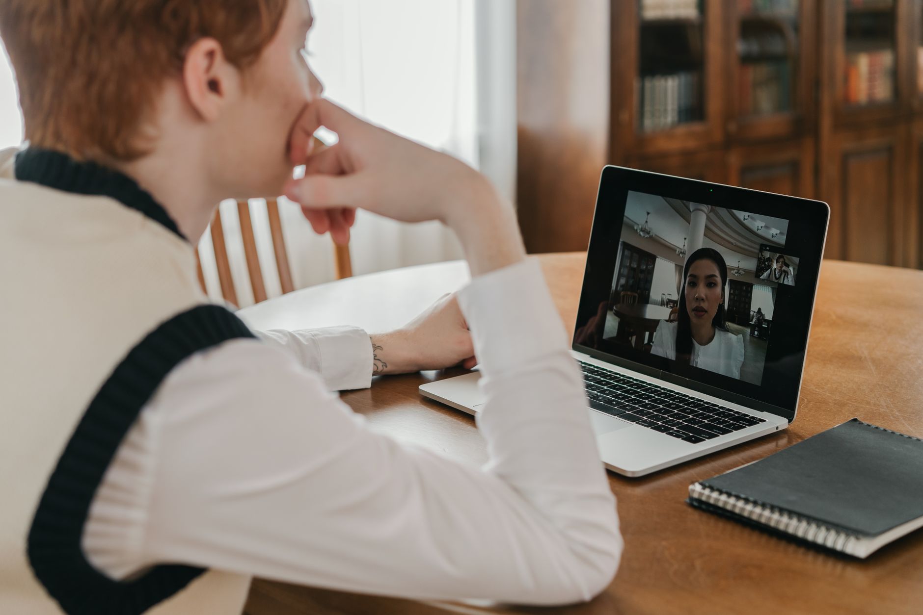 Jeune homme assis à une table en bois lors d'un appel vidéo avec une femme affichée sur l'écran d'un ordinateur portable