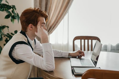 Free Young man focused on studying at home with a laptop, surrounded by natural light and decor. Stock Photo