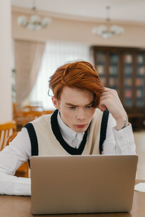 Free Red-haired young man studying intently in a cozy indoor setting with a laptop. Stock Photo