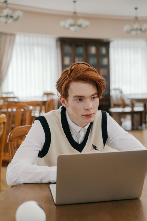 Free Young man focused on studying online in a library, using a laptop for learning. Stock Photo