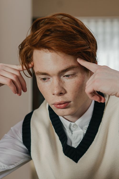 Free A thoughtful young man with red hair contemplating ideas while seated indoors. Stock Photo