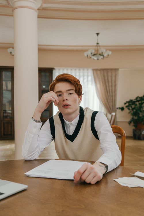 Free A thoughtful young man sitting at a table with papers, indoors, studying. Stock Photo