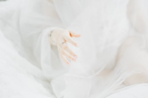 Free Crop anonymous gentle female with ring on finger sitting in light room at home covered with delicate translucent white cloth Stock Photo