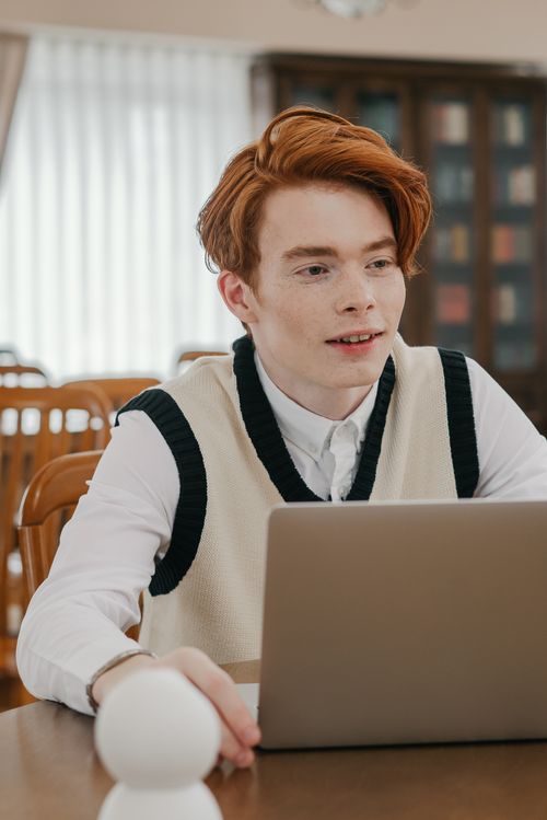 Free Focused young man using a laptop in a cozy library, engaging in online learning and studying. Stock Photo