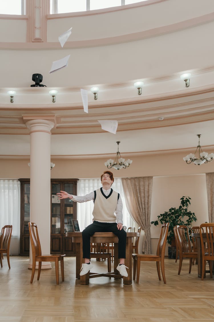 Young Man Sitting On Table Throwing Papers