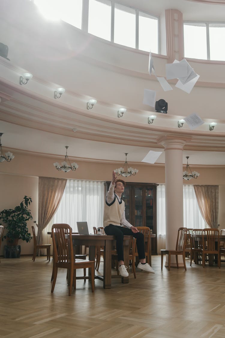 A Man Throwing Papers In The Air While Sitting On A Table