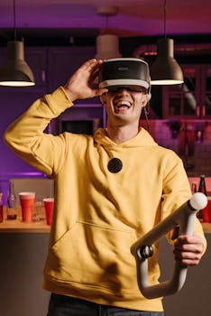 A young man in a yellow hoodie enthusiastically playing with a VR headset indoors.