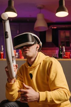 Man plays immersive virtual reality game indoors wearing a VR headset and yellow hoodie.