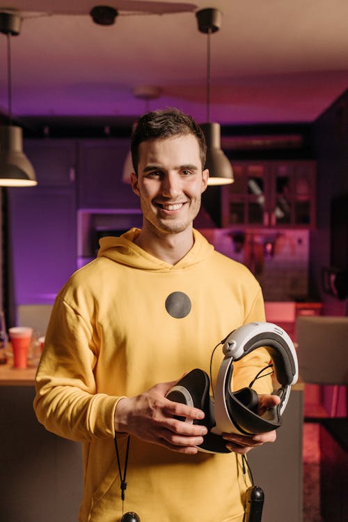 A Man in a Yellow Hoodie Holding a VR Headset and Game Controllers