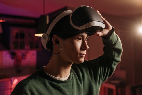 Free A man in a green sweater adjusts his VR headset while experiencing virtual reality indoors. Stock Photo