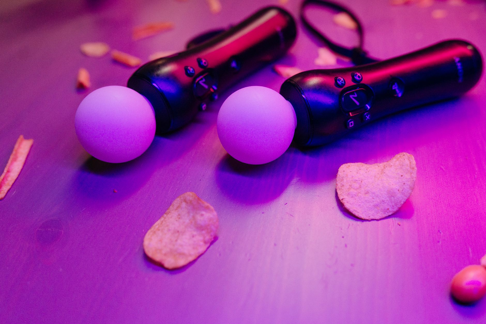 Close-up of video game controllers with potato chips under neon pink lighting.