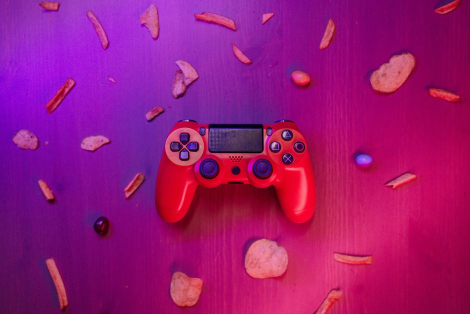 Stylish red game controller surrounded by snacks on a vibrant purple background.