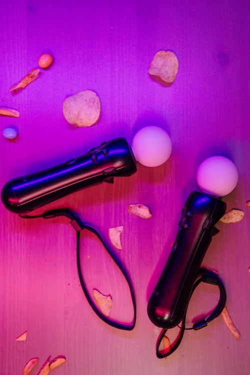 Free Two handheld gaming controllers on a table with scattered potato chips under neon lights. Stock Photo