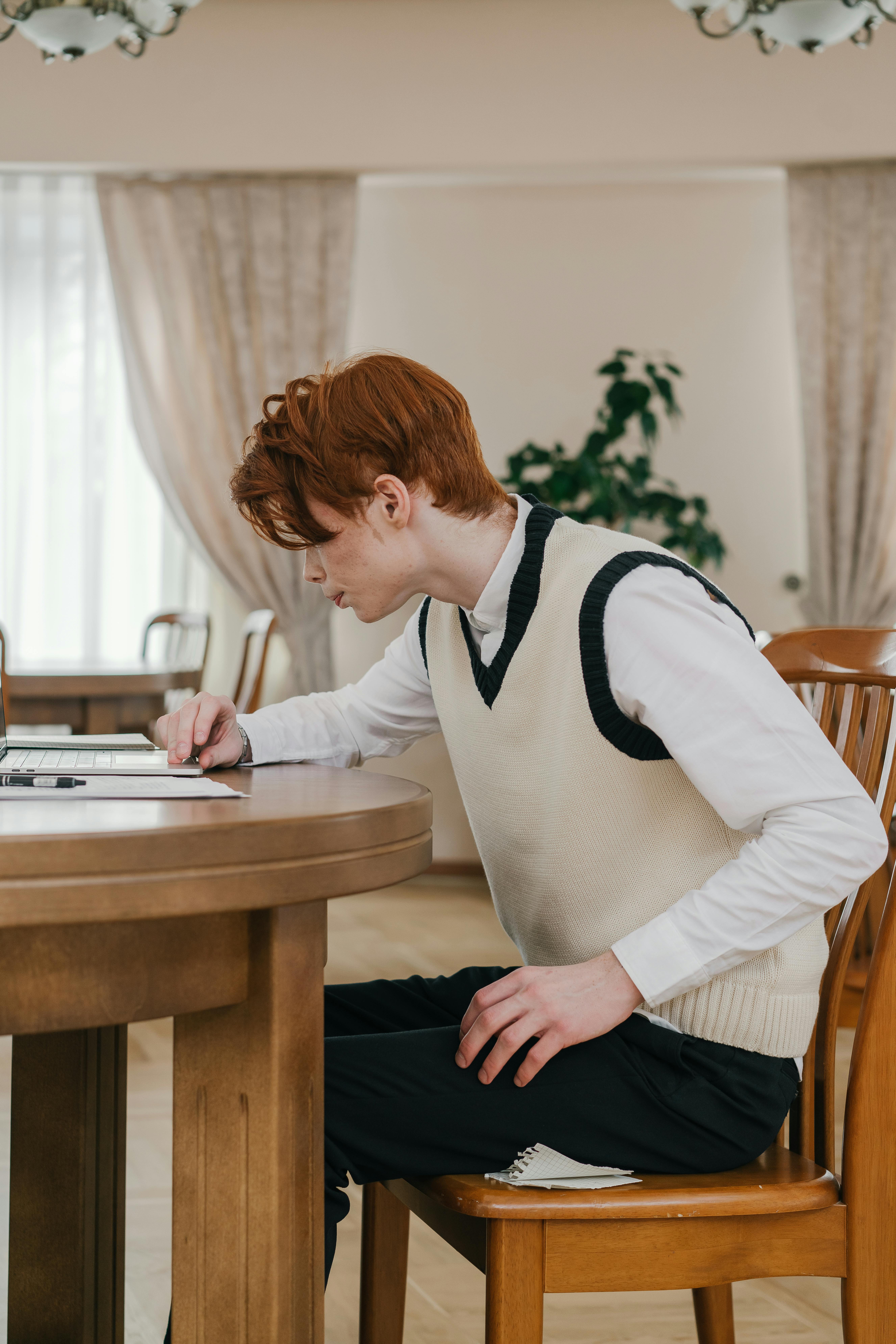 A young adult man with red hair studies intently indoors at a wooden table.