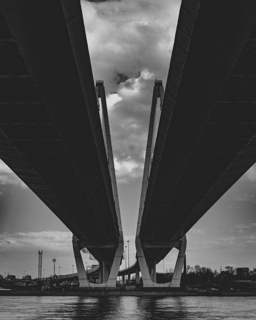 Free Dramatic black and white photo of a symmetrical bridge with clouds in the sky. Stock Photo