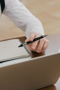 Hand holding a pen over a notepad near a laptop, capturing a work or study moment.