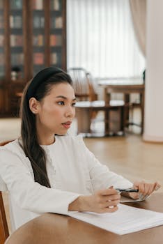 Asian woman studying with focus, holding pen in library setting.