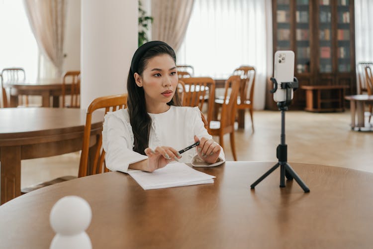 A White Long Sleeves Sitting Near The Wooden Table While Looking At Her Mobile Phone