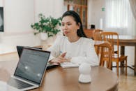 A Woman in White Long Sleeves Sitting Near the Laptops on a Wooden Table