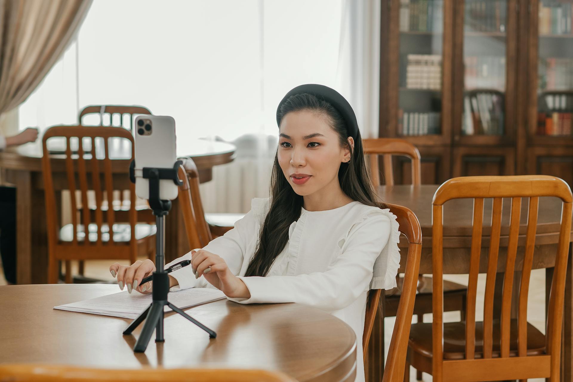 A Woman in White Long Sleeves Sitting on a Wooden Chair while Talking on the Phone