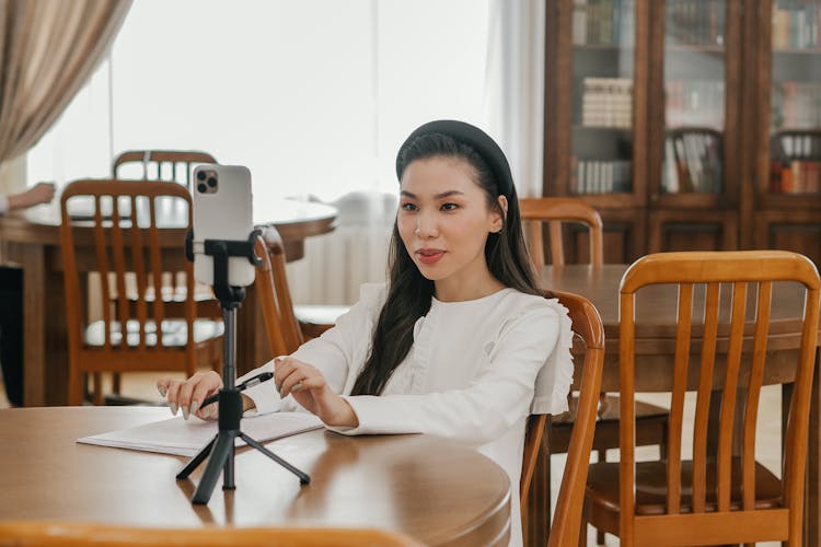 A Woman In White Long Sleeves Sitting On A Wooden Chair While Talking On The Phone