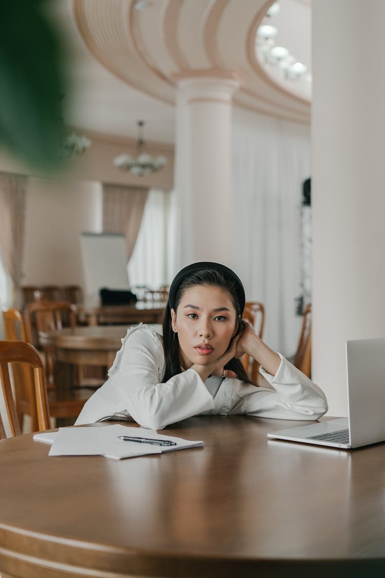 A Woman In White Long Sleeves Sitting Near The Laptop On A Wooden Table