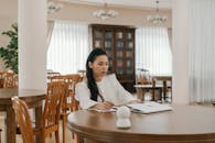 A Woman in White Long Sleeves Sitting Near the Laptop on a Wooden Table