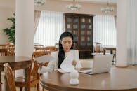 A Woman in White Long Sleeves Sitting on a Wooden Chair while Holding Papers