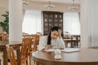 A Woman in White Long Sleeves Looking at the Paper on the Table with Her Hand on Her Head