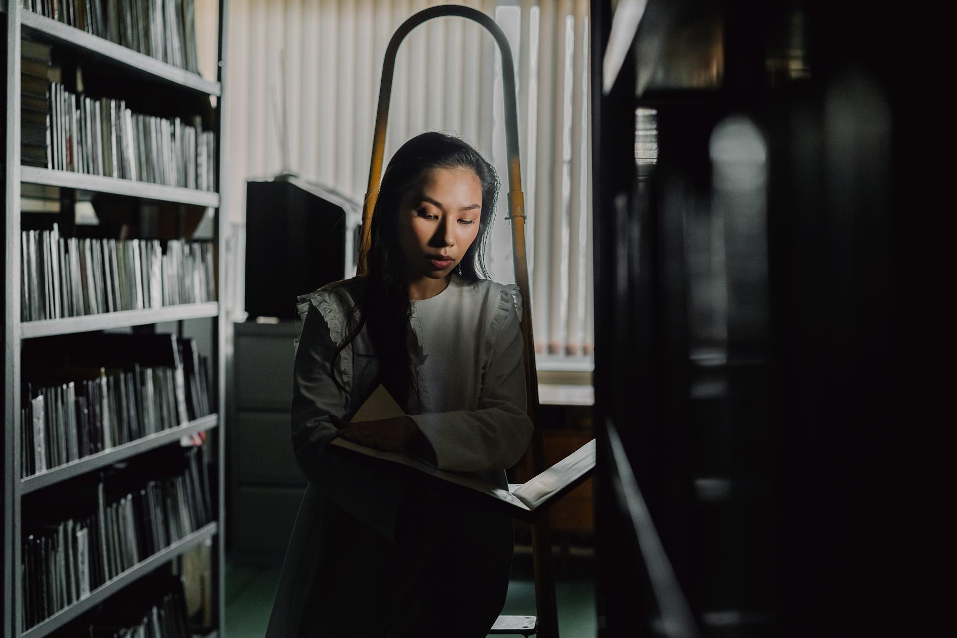 A woman deeply absorbed in a book within the dim light of a quiet library.