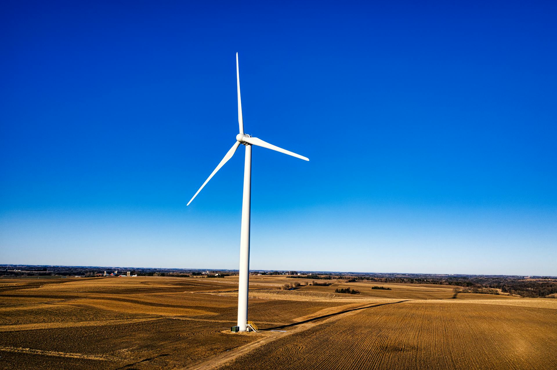 A solitary wind turbine stands against a blue sky in the fields of Altura, Minnesota, reflecting sustainable energy.