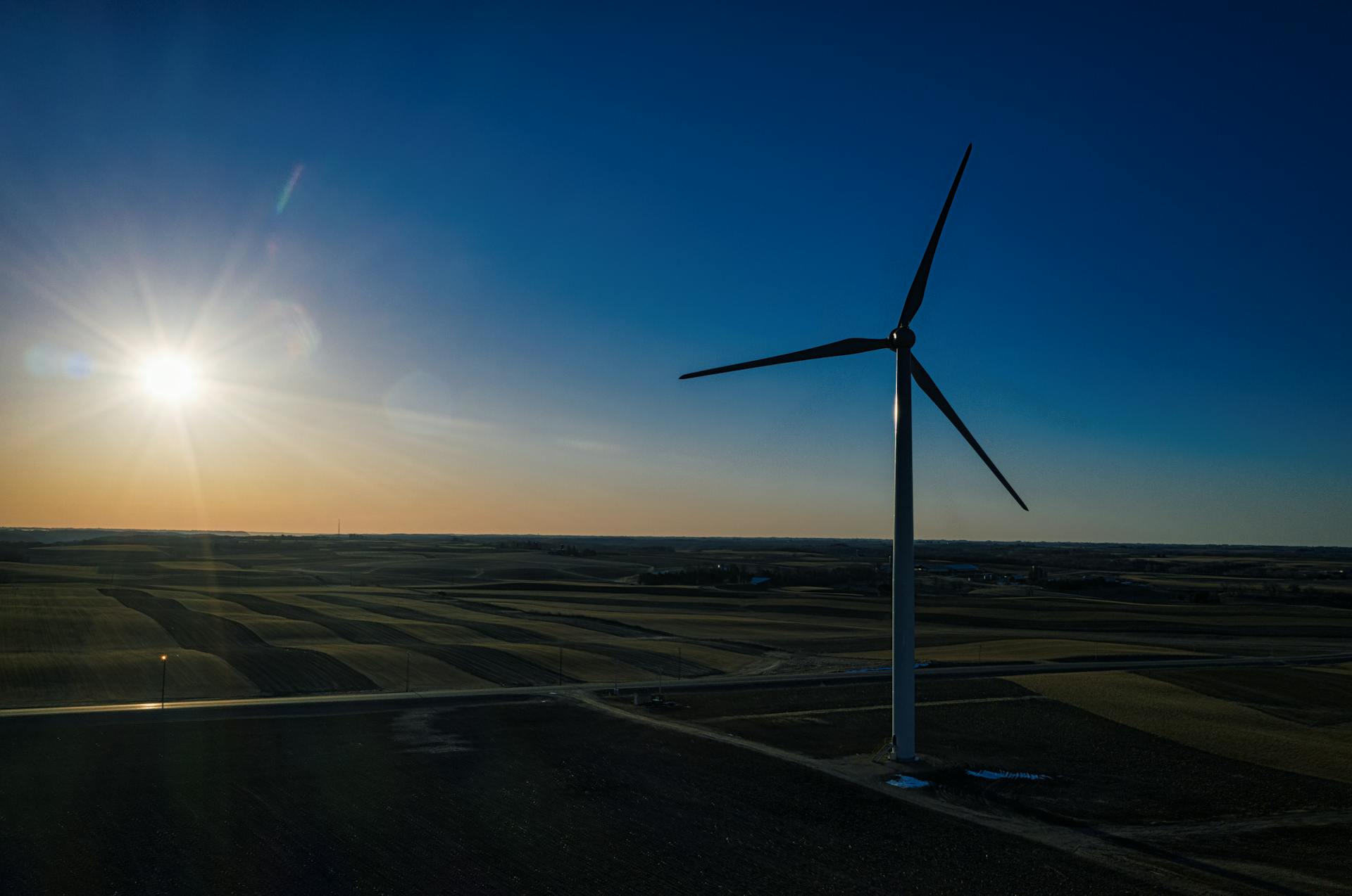 Wind turbine in Altura, MN with sun glare and vast countryside landscape.