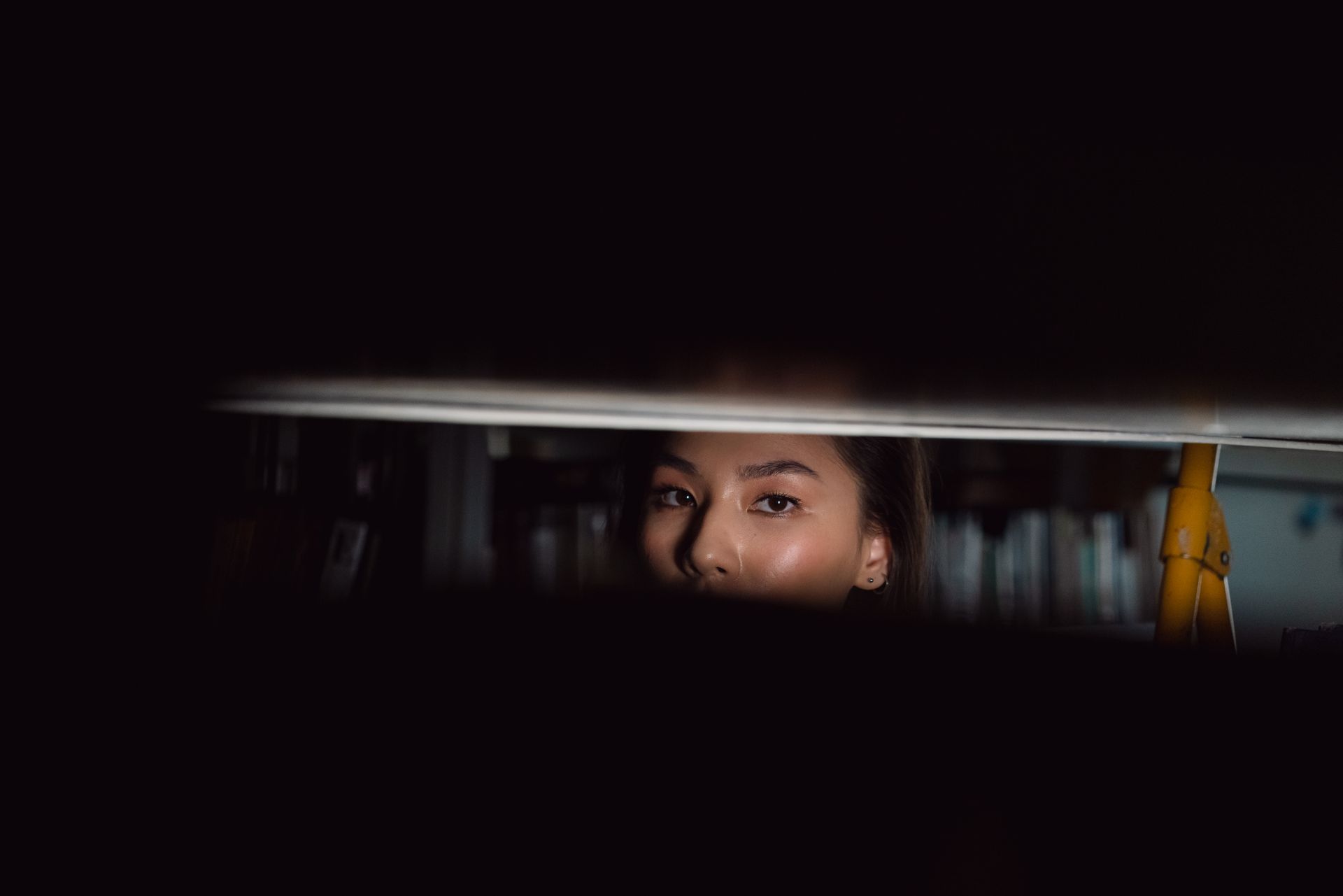 A woman's eyes peek through blinds in a mysterious and atmospheric setting.