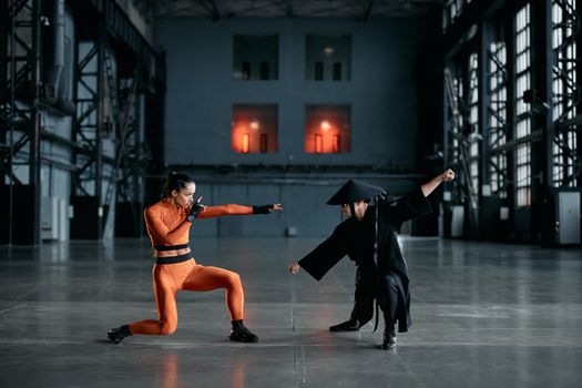 Two performers engaged in martial arts poses in a spacious industrial hall, creating a dynamic scene.