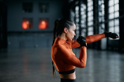 Free Side view of a woman in orange activewear practicing boxing indoors, exuding focus and determination. Stock Photo
