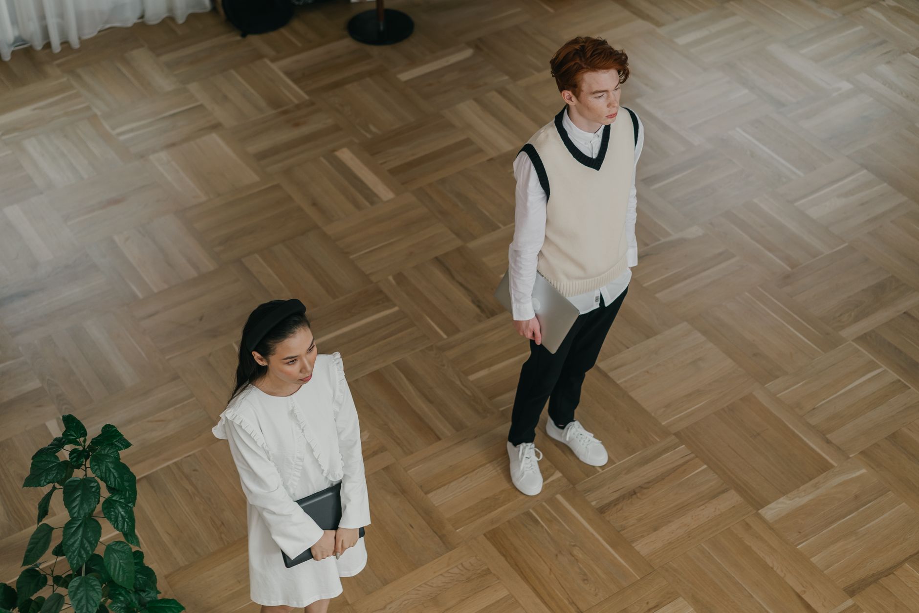 High angle view of two young adults in a minimalist indoor space featuring wooden flooring.