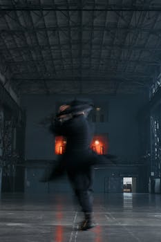 A blurred figure in black moves swiftly indoors under high industrial ceilings.